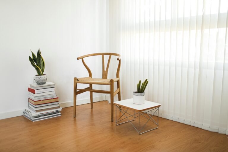 A minimalist room with wooden chair, books, and potted plants by the window.
